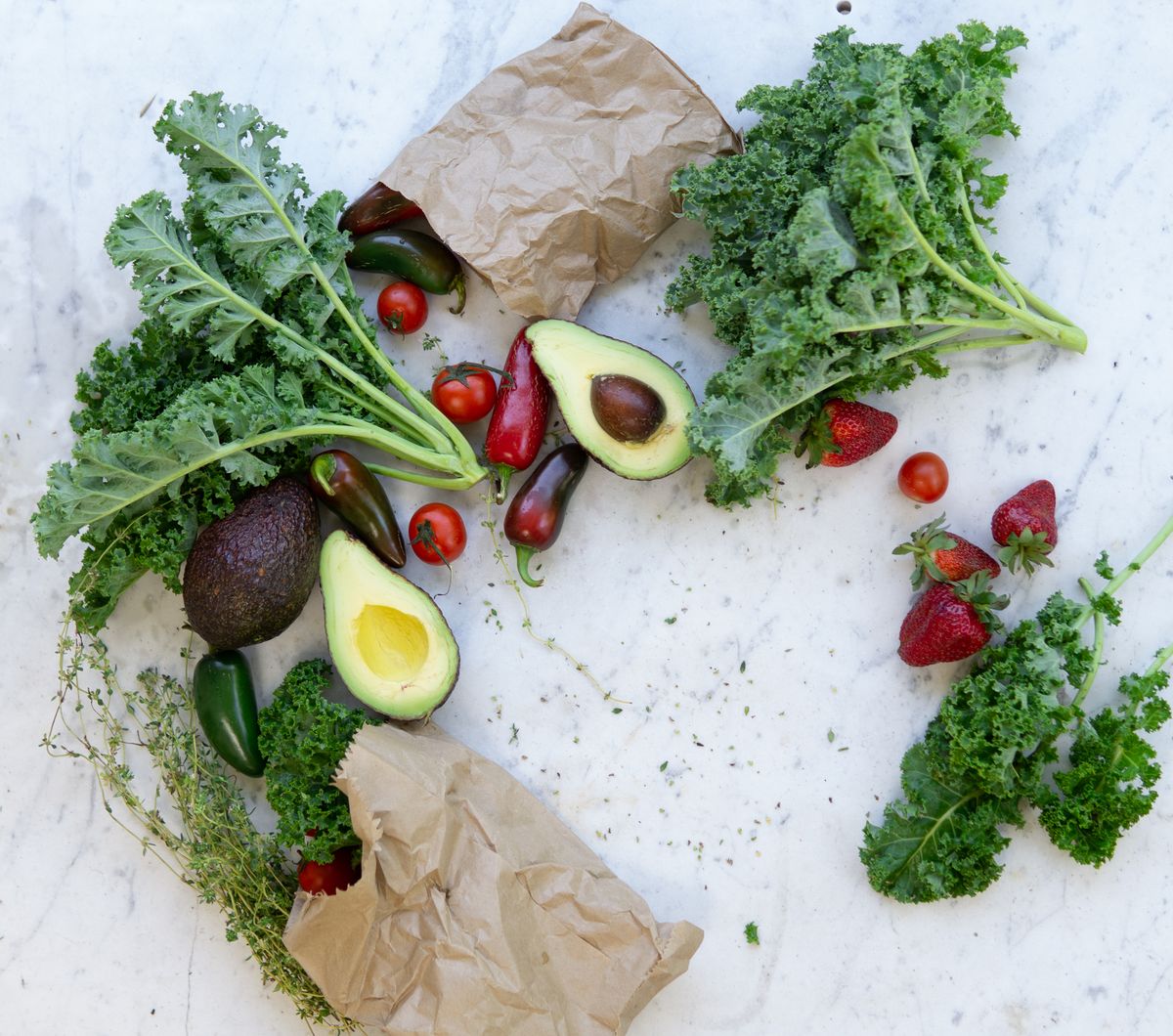 Fresh kale, avocados, strawberries, tomatoes and peppers laid out on a marble counter