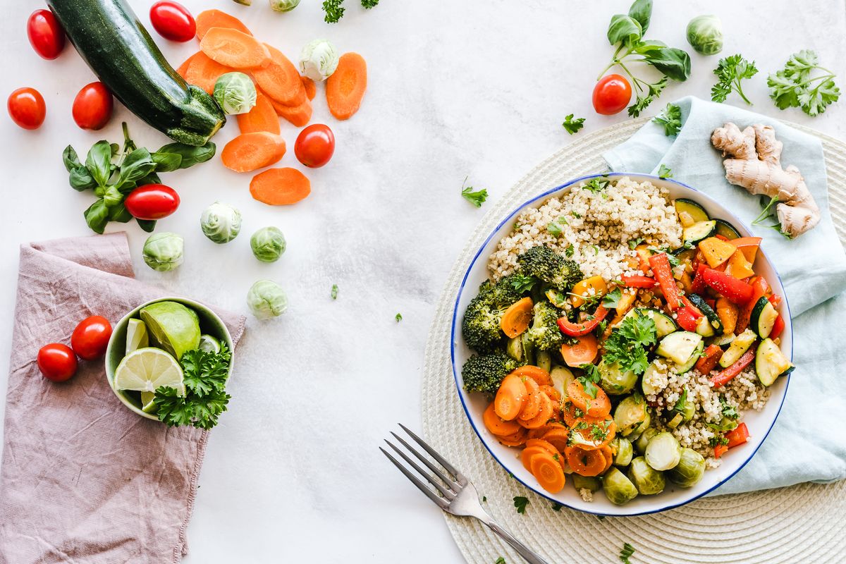 A colourful bowl of quinoa, roasted vegetables, carrots and greens surrounded by fresh ingredients